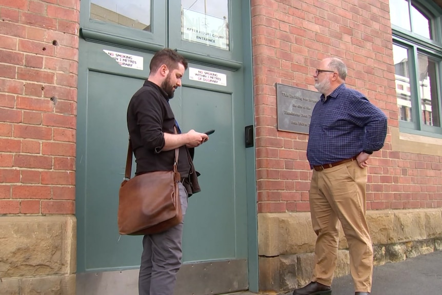 Two male journalists stand outside the locked after-hours entrance to the Hobart Magistrates Court