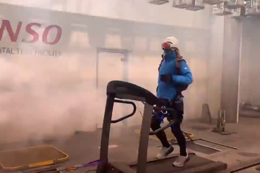 Woman wearing winter gear and goggles running on treadmill in a room with strong wind being blown at her