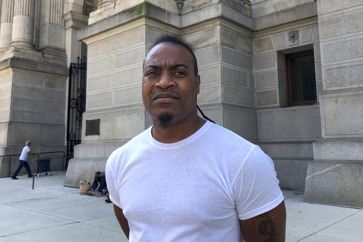 Mark St. Bernard stands on a sidewalk in front of a building.