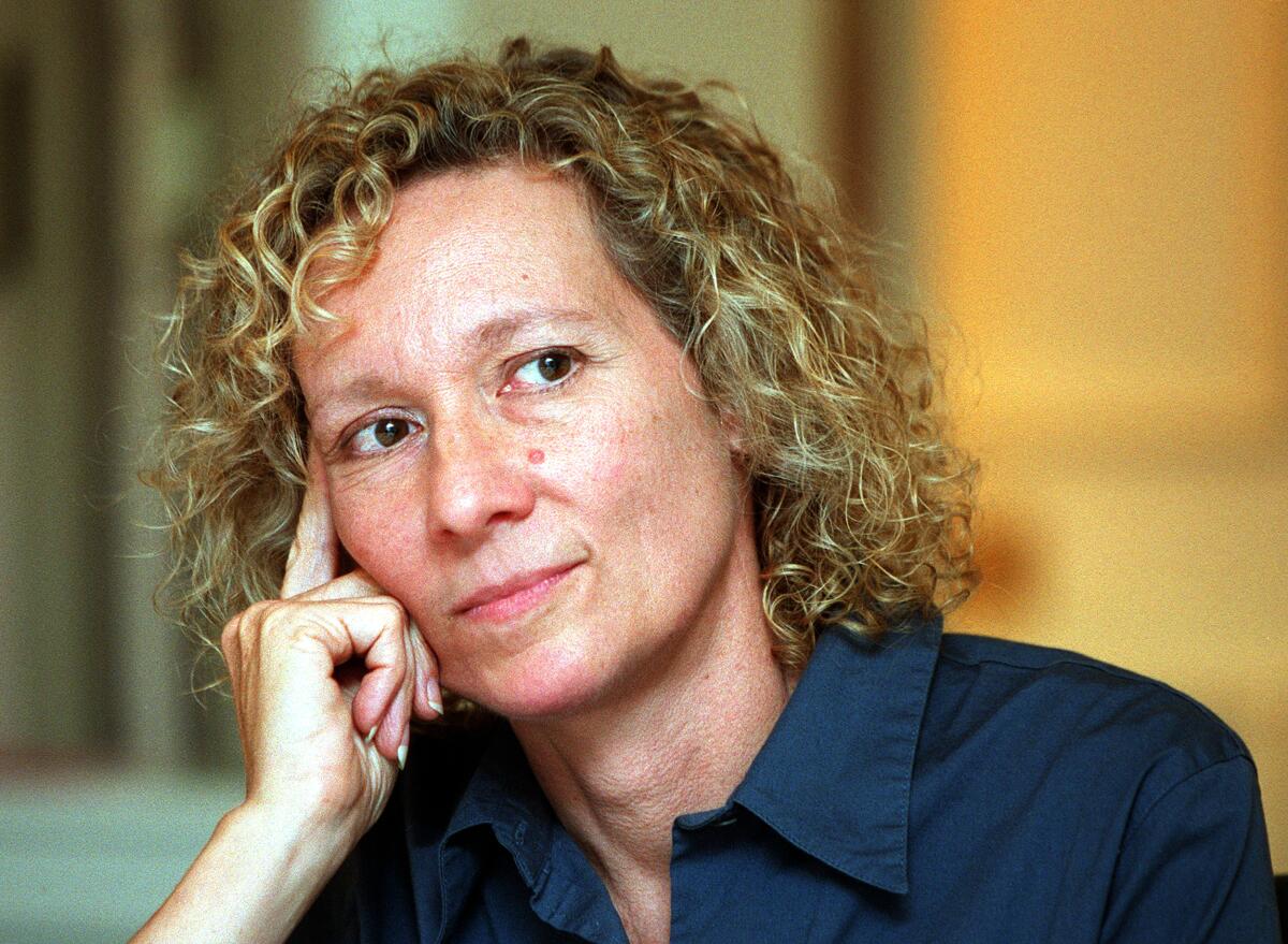 Artist Alexis Smith, a white woman with blond, curly hair, leans her head on her hand in a portrait from 1999.