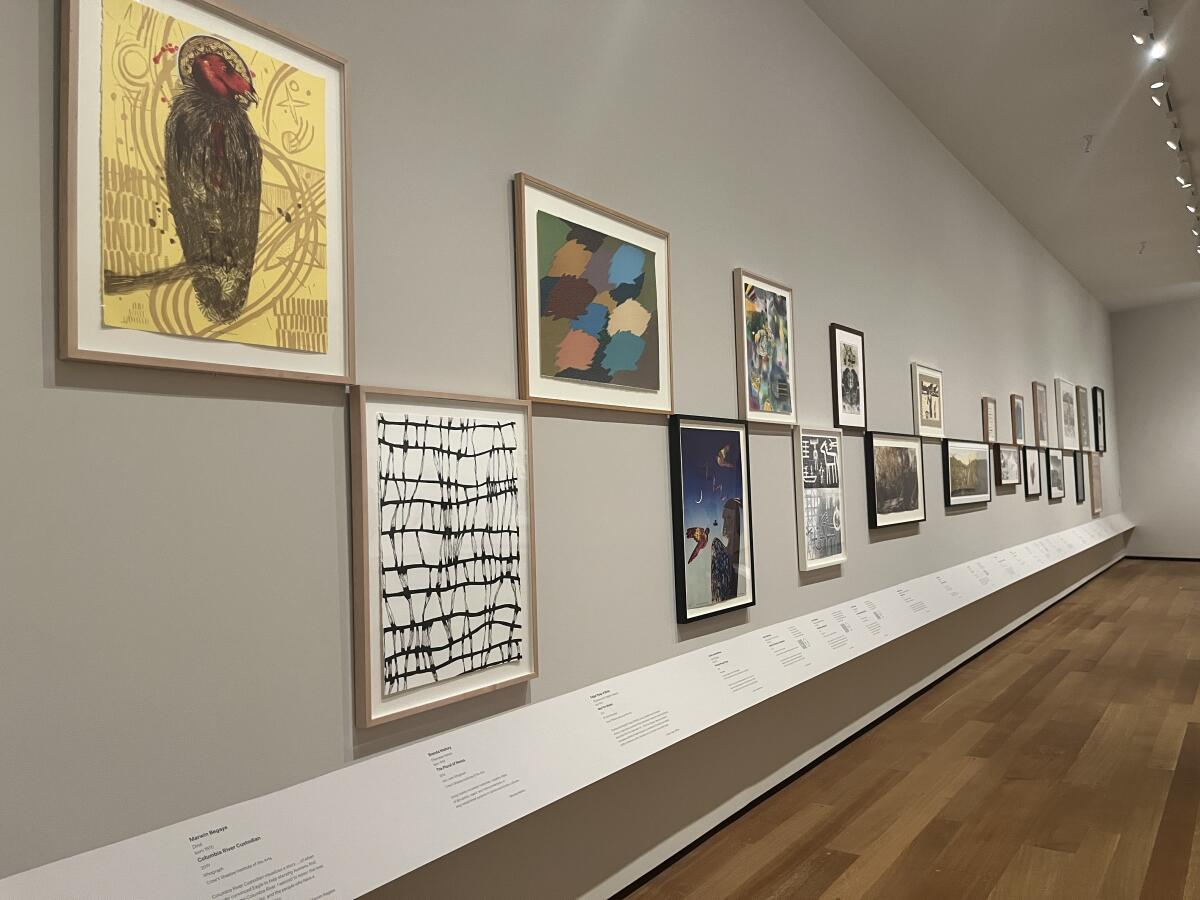 A view of a gallery shows paintings and prints laid out in a checkerboard pattern against a gray wall.