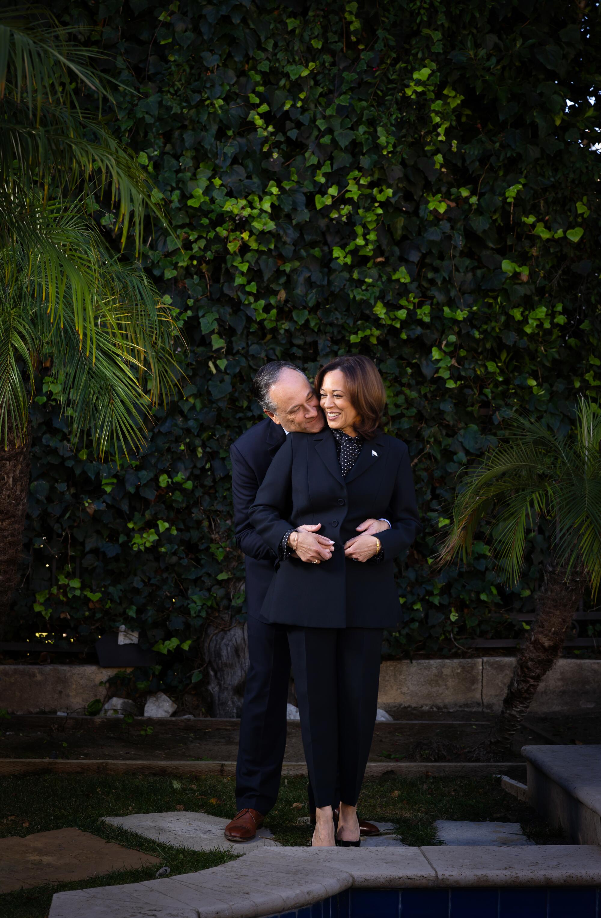 Kamala Harris stands outside while Doug Emhoff stands behind her and rests his chin on her shoulder.