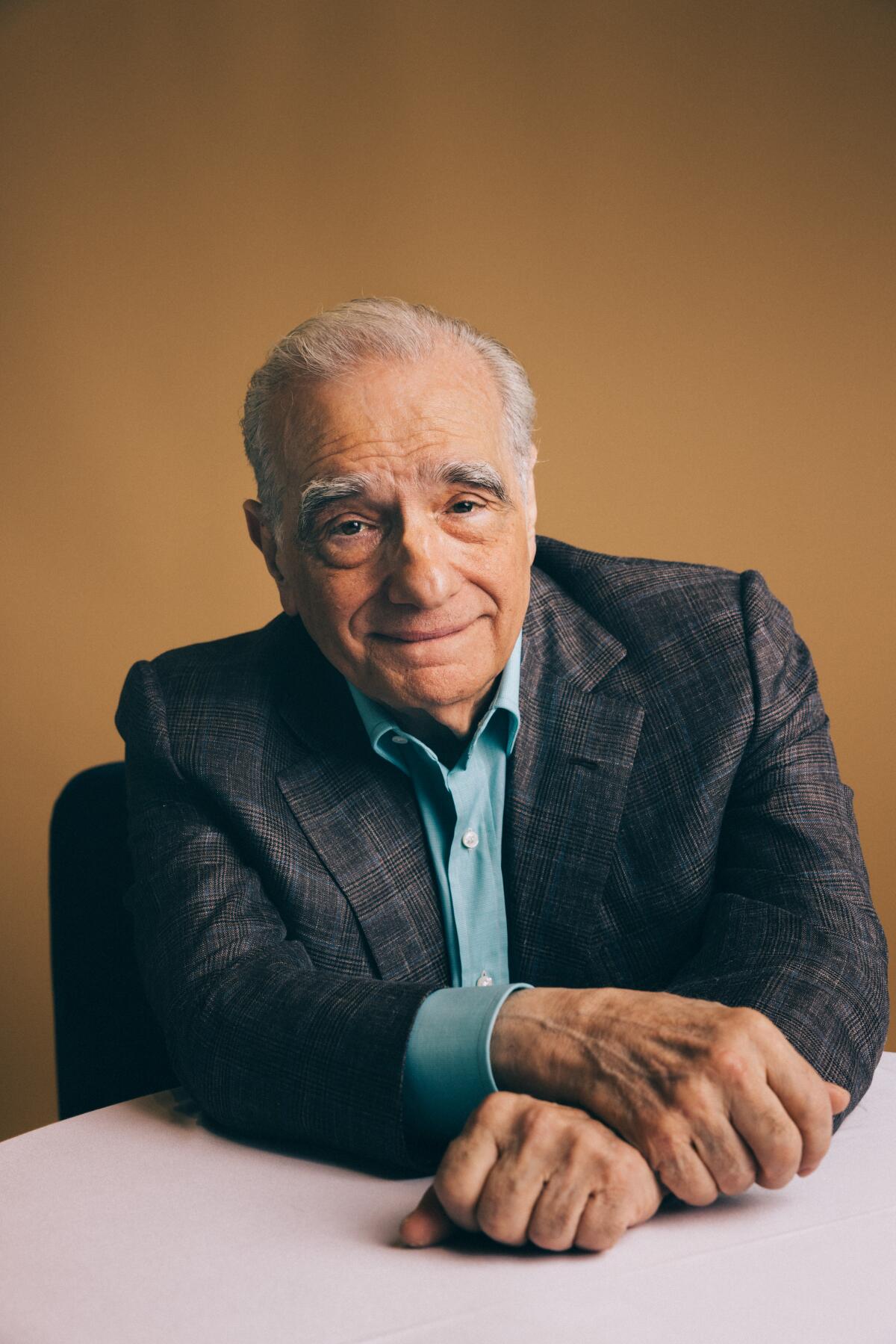 Martin Scorsese rests his arms on the table before him for a portrait.