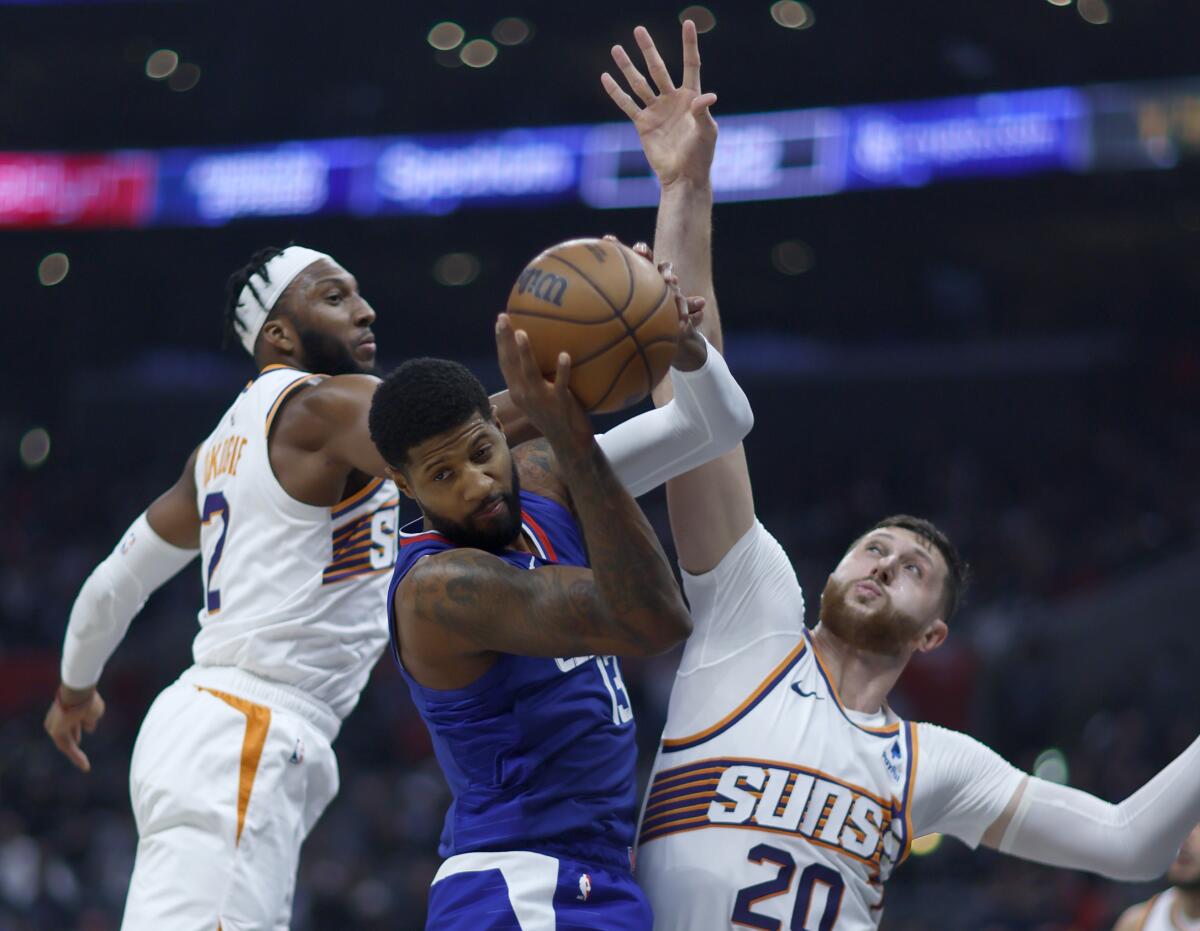 Clippers forward Paul George, center, grabs a rebound between Phoenix’s Josh Okogie, left, and Jusuf Nurkic.