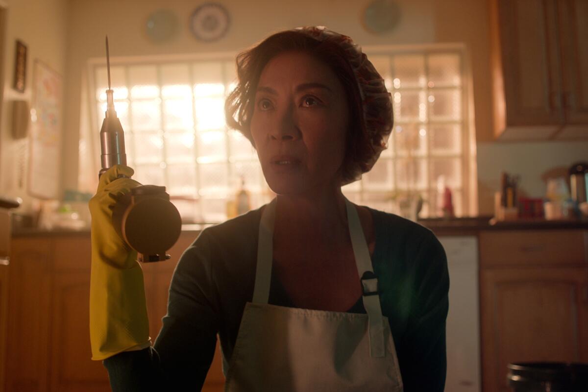 A woman wearing yellow rubber gloves and an apron holds up an electric saw.