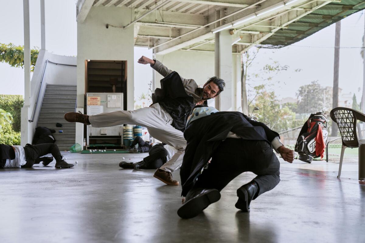 A man in white pants stands with an outstretched leg as another man in black falls toward the ground.