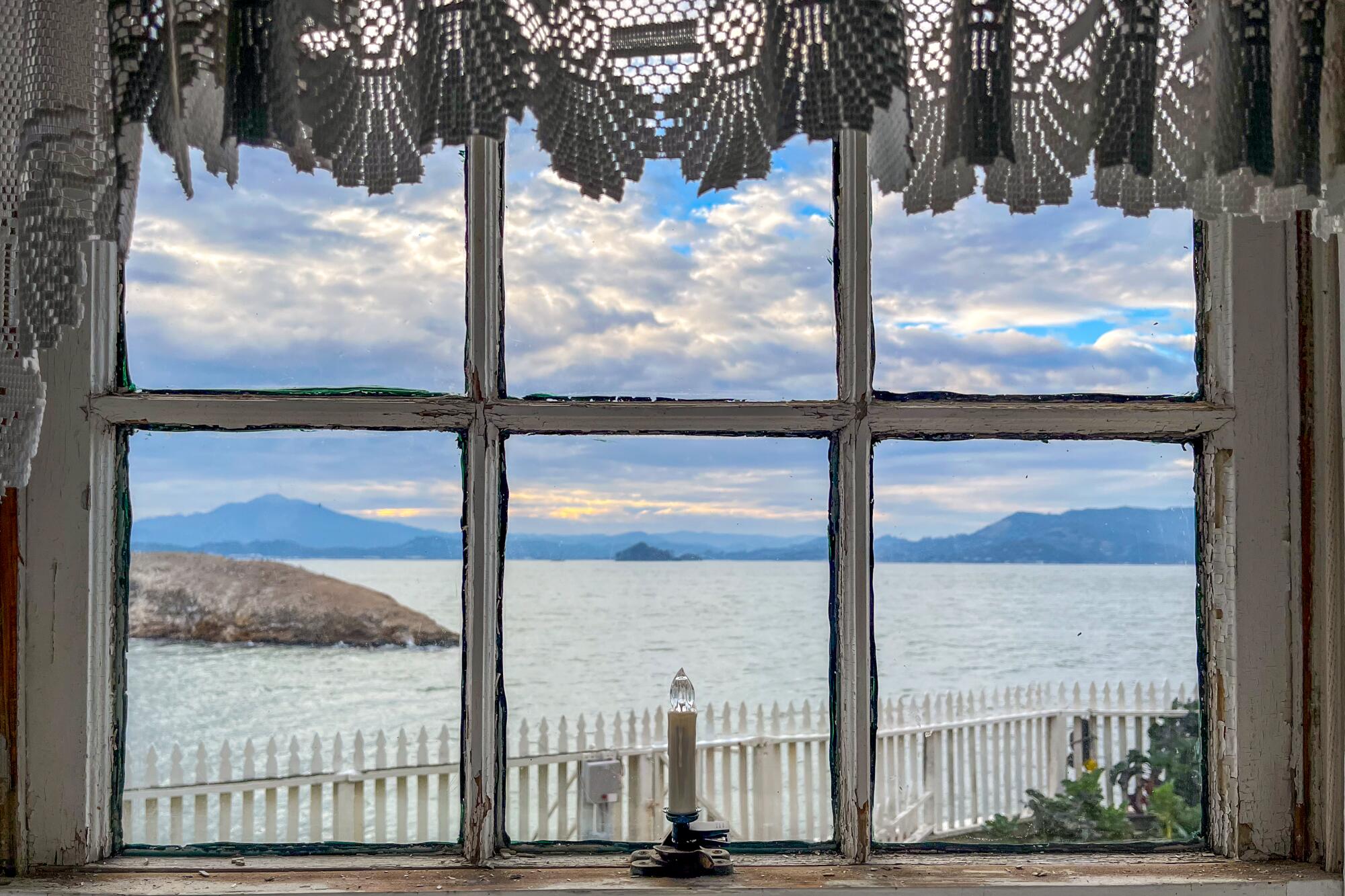 A view out a window of a white picket fence, greenery and the bay.