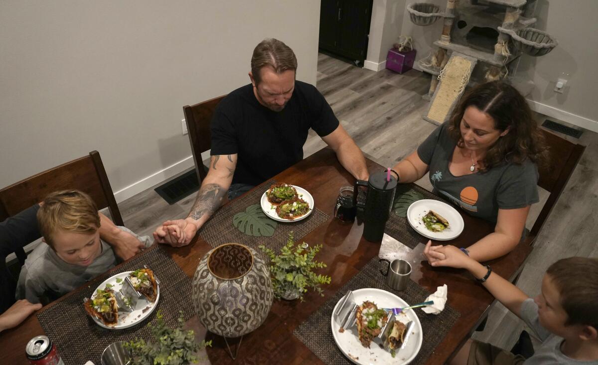 Family members hold hands at a table while saying a prayer