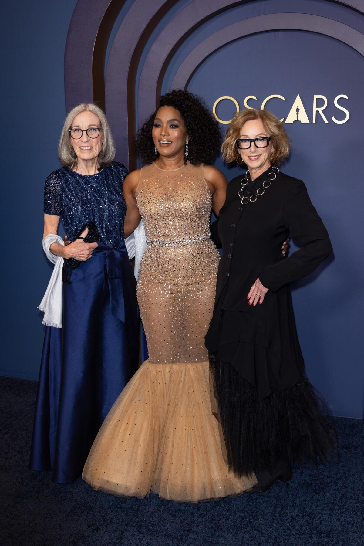 Three women in glamorous clothing pose for the camera.