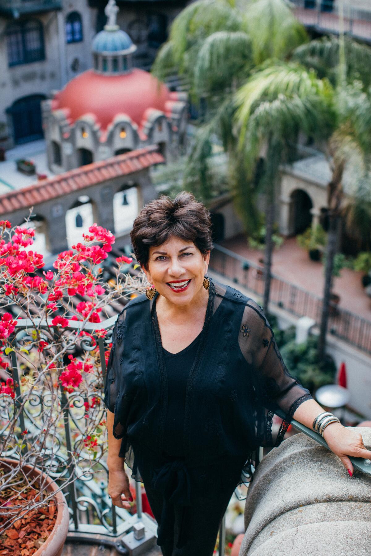 Ofelia Valdez-Yeager, a Latina woman dressed in black, stands before flowers and a domed rooftop.