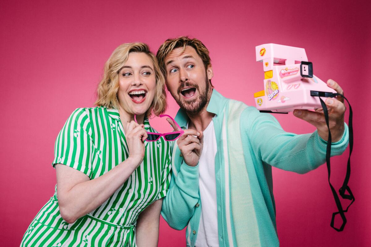 Greta Gerwig and Ryan Gosling playfully pose for a selfie with a pink Polaroid camera.
