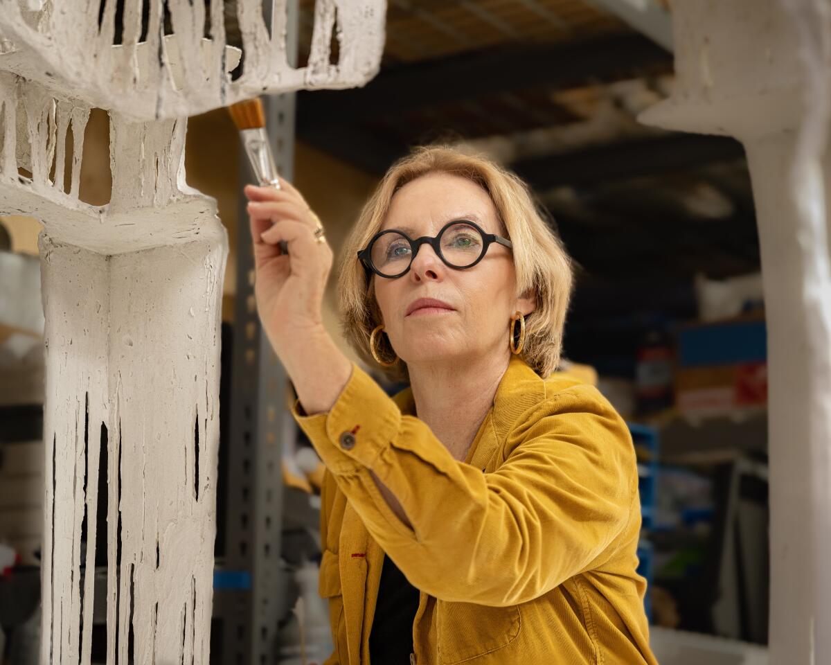 Rosa Lowinger, an art restorer and author in a mustard shirt, holds a paintbrush to an old work she is restoring.