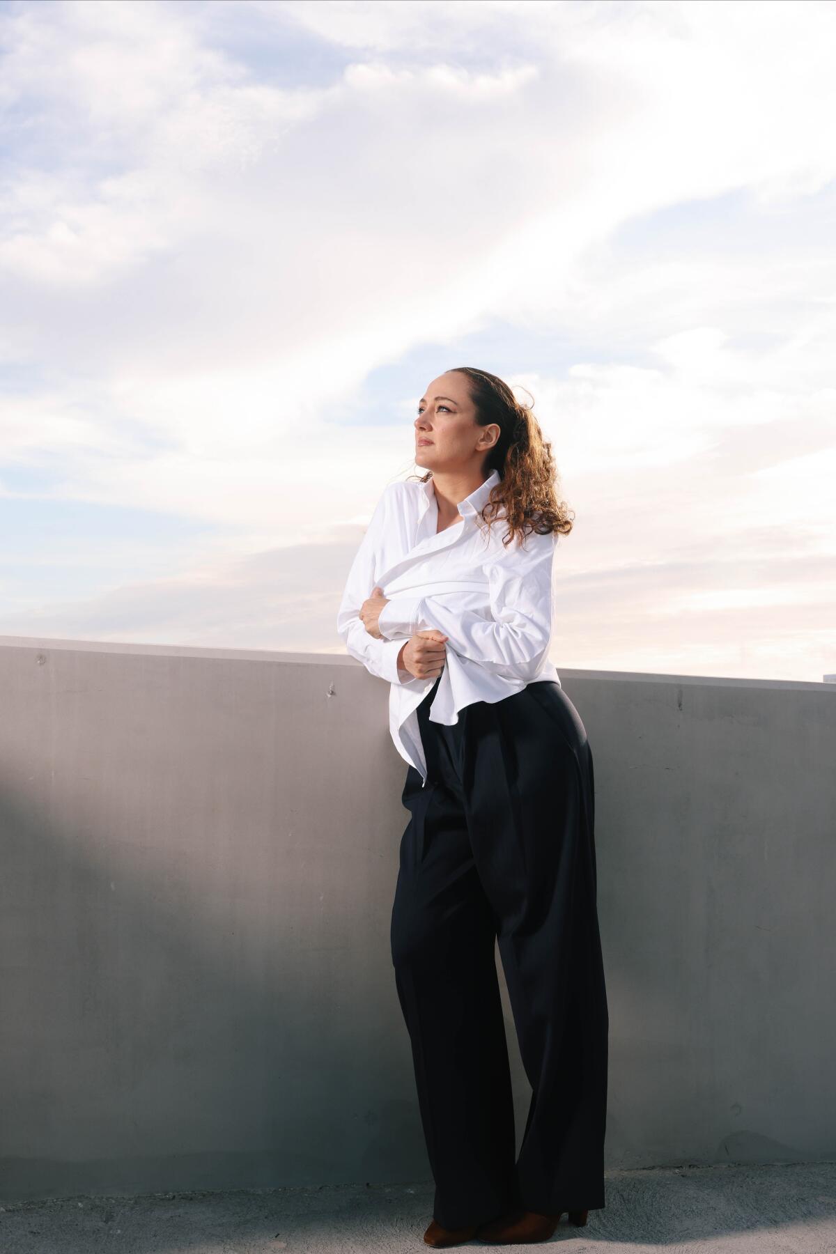 Woman stands leaning against a wall