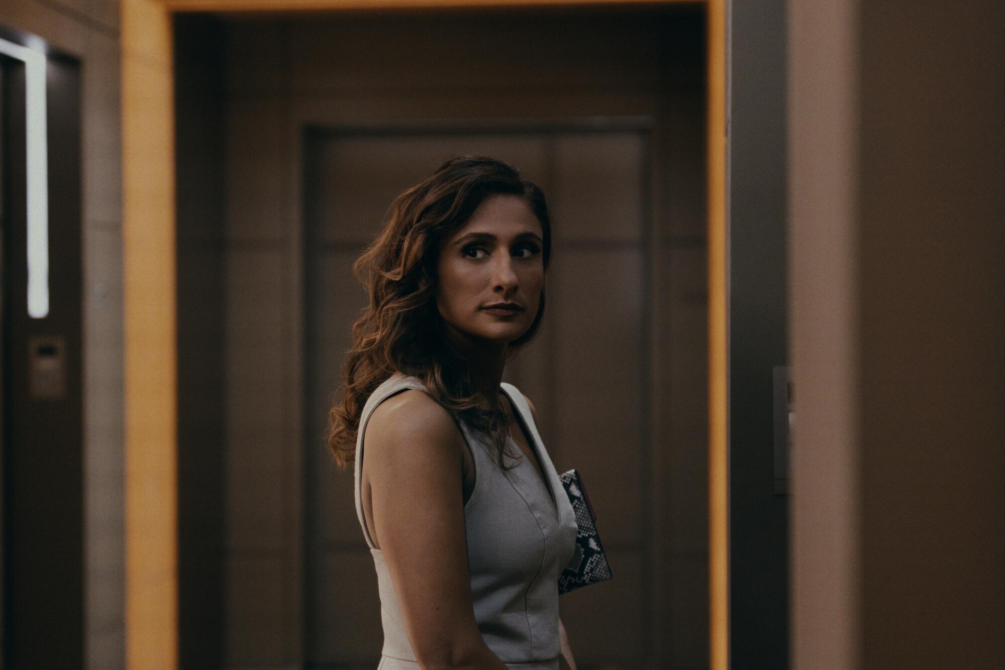 A woman in a sleeveless white top stands in a hallway.