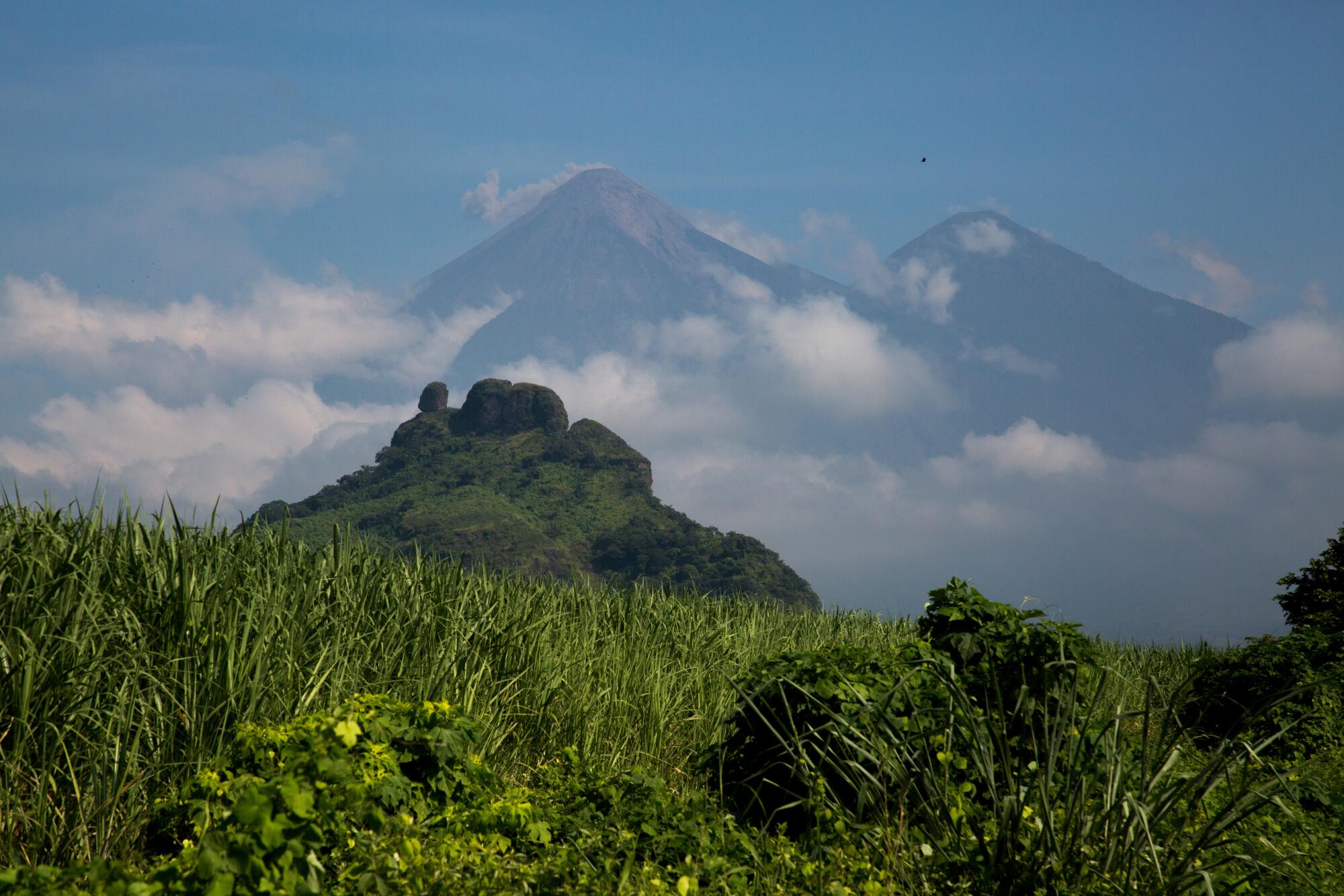 A grassy meadow with an erupting volcano, with two mountains in the background