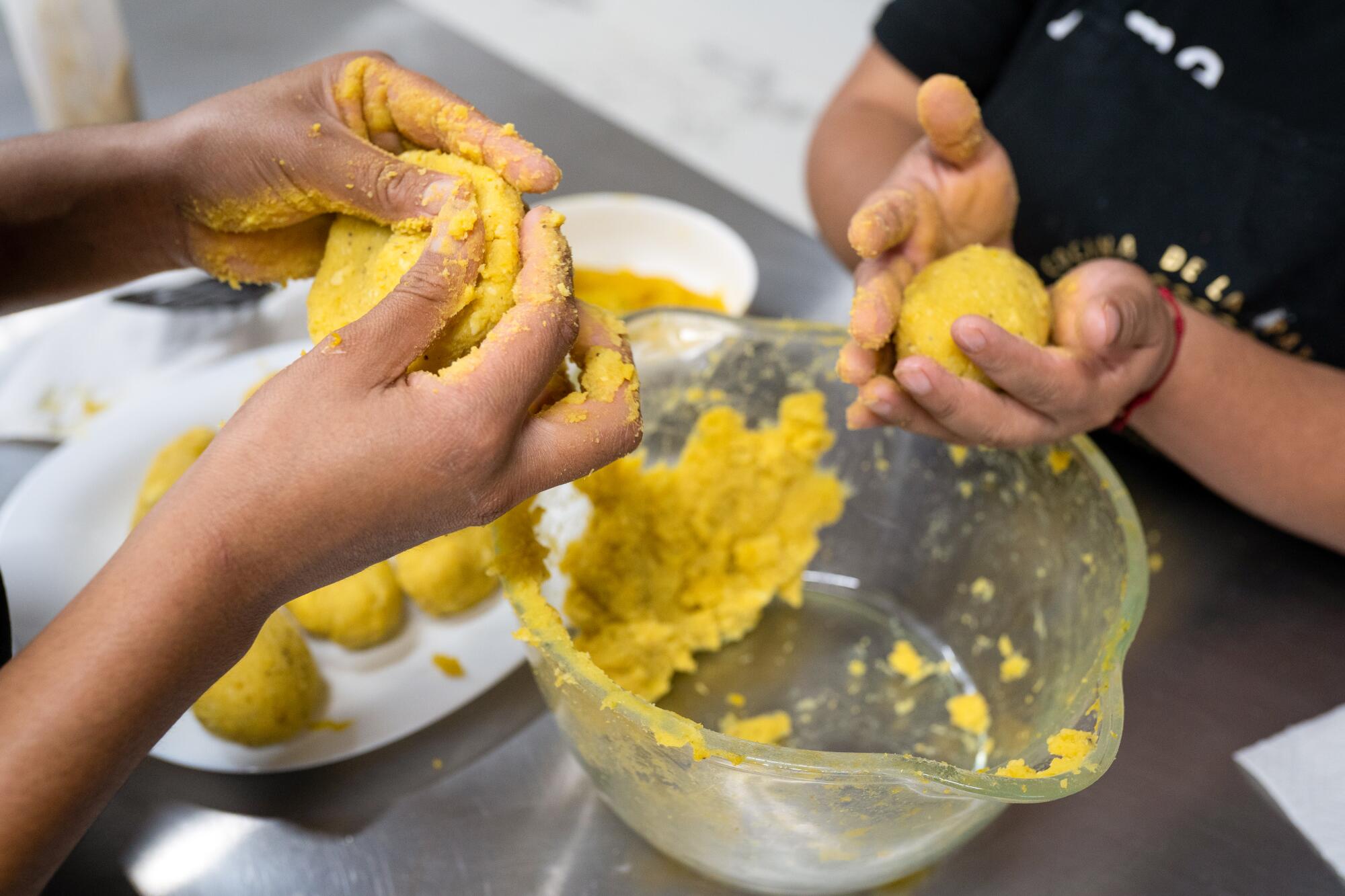 Two pairs of hands flattening and rolling a yellow mush into shapes.