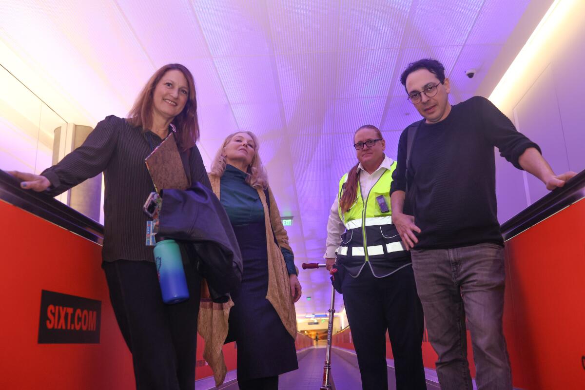 Four people ride a moving sidewalk under a purple-lighted ceiling