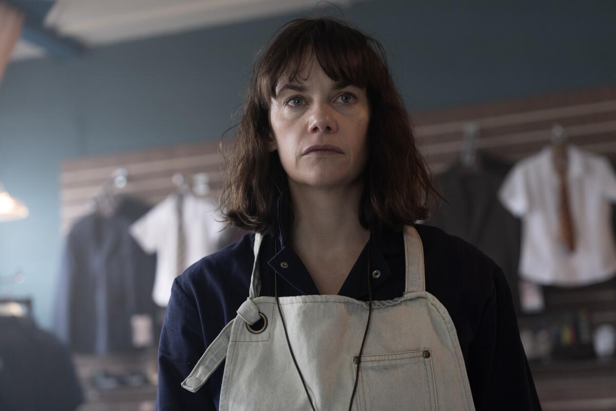 A brown-haired woman in a blue shirt and white apron.