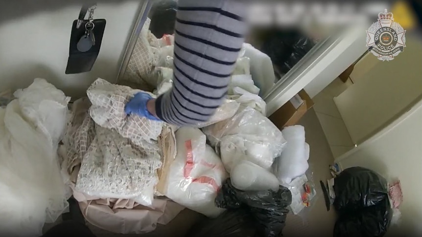 arm of detective sifting through pile of wedding dresses on floor