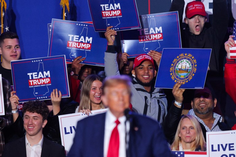 Supporters of Donald Trump cheer as he speaks at a podium during a rally in New Hampshire