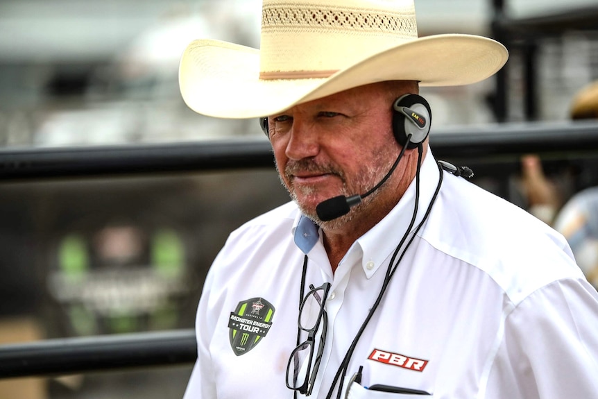 A middle aged man wearing a light coloured cowboy hat and white shirt and wearing a microphone headpiece.