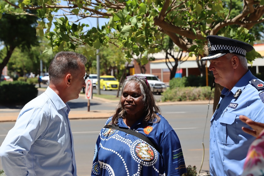 An Indigenous woman stands between a man in shirt and a police officer