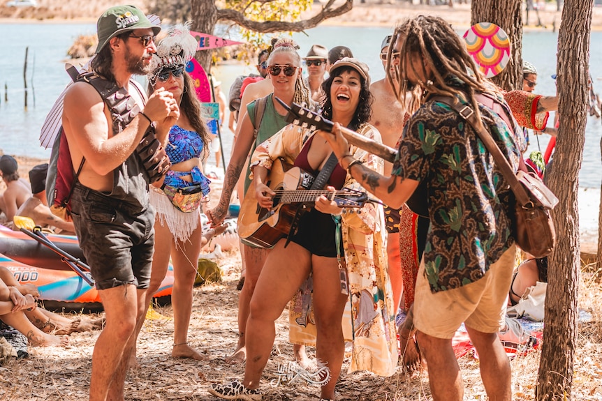 A man and woman stand playing guitars as people dance around. 