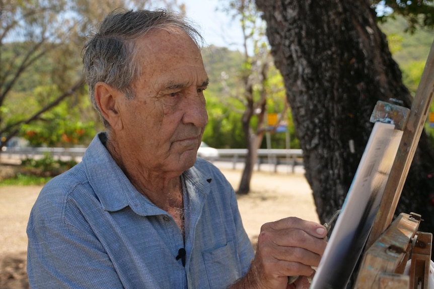 Man stands in front of canvas and paints. 