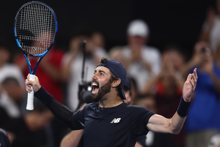 Jordan Thompson smiling with his arms up holding a tennis racket. 