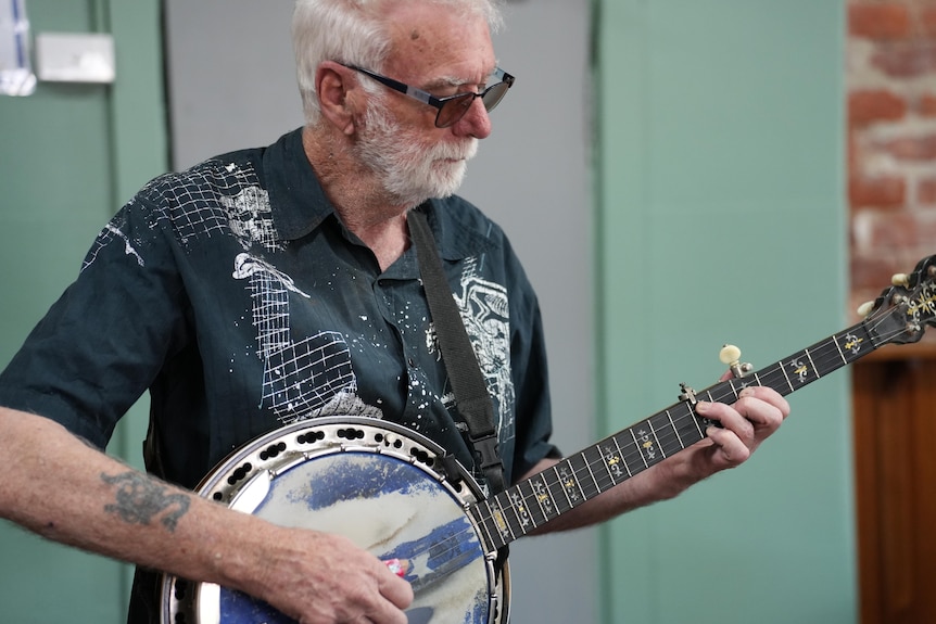 A man in a black and white shirt playing a banjo.