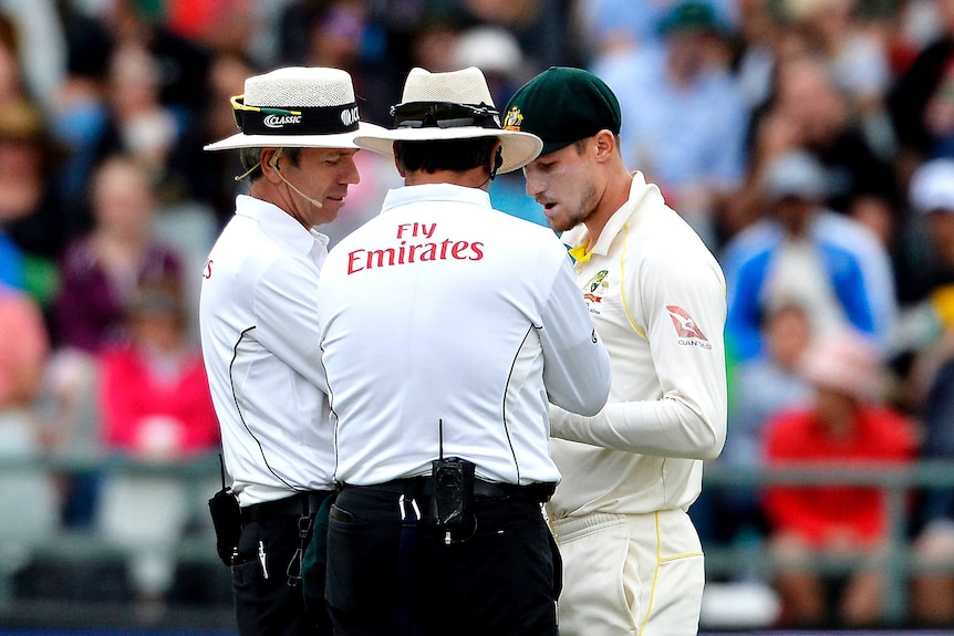 Telephoto shot of two umpires and a cricketer standing and talking onfield.