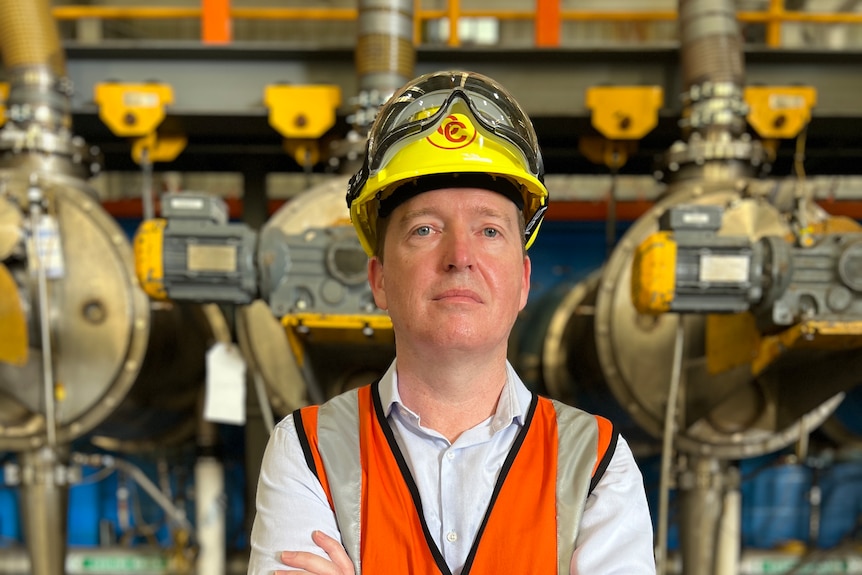 A man wearing a high-vis vest and hard hat looks straight at the camera. 