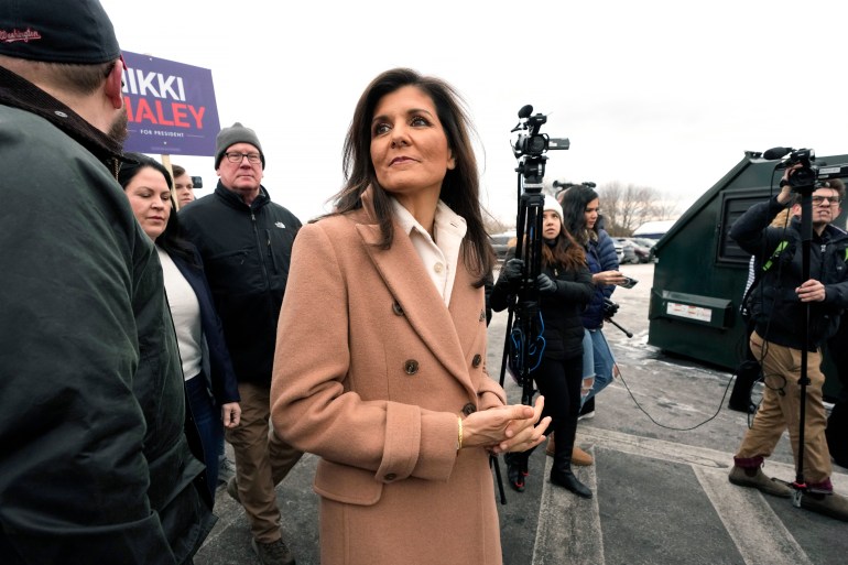 Nikki Haley, in a light brown pea coat, stands outside with supporters in New Hampshire.