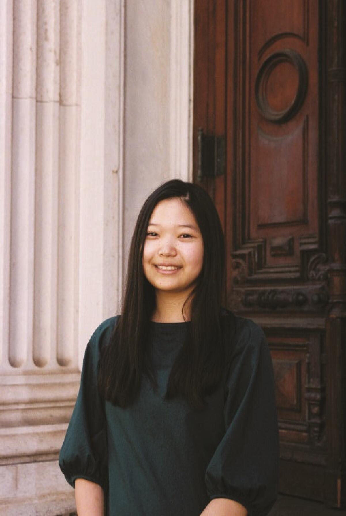 A woman in black stands by a carved wood door and a fluted concrete pilaster.