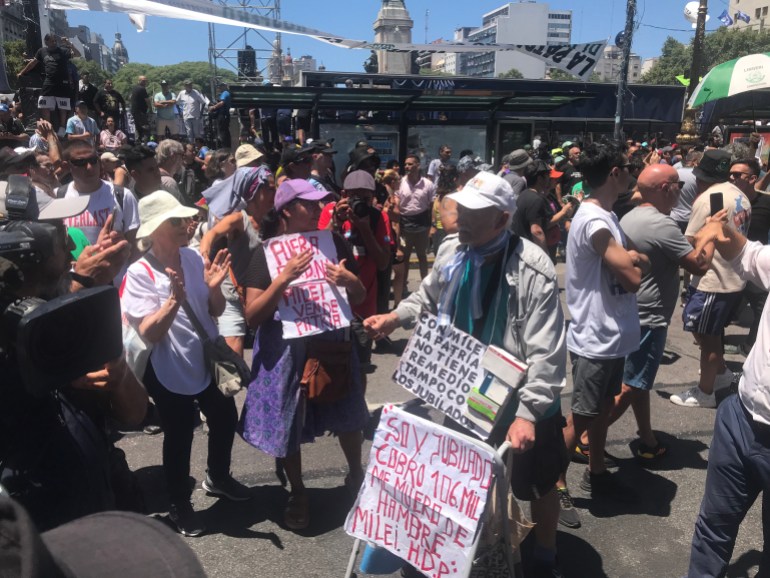 A protester holds a handwritten sign among a street of fellow demonstrators.