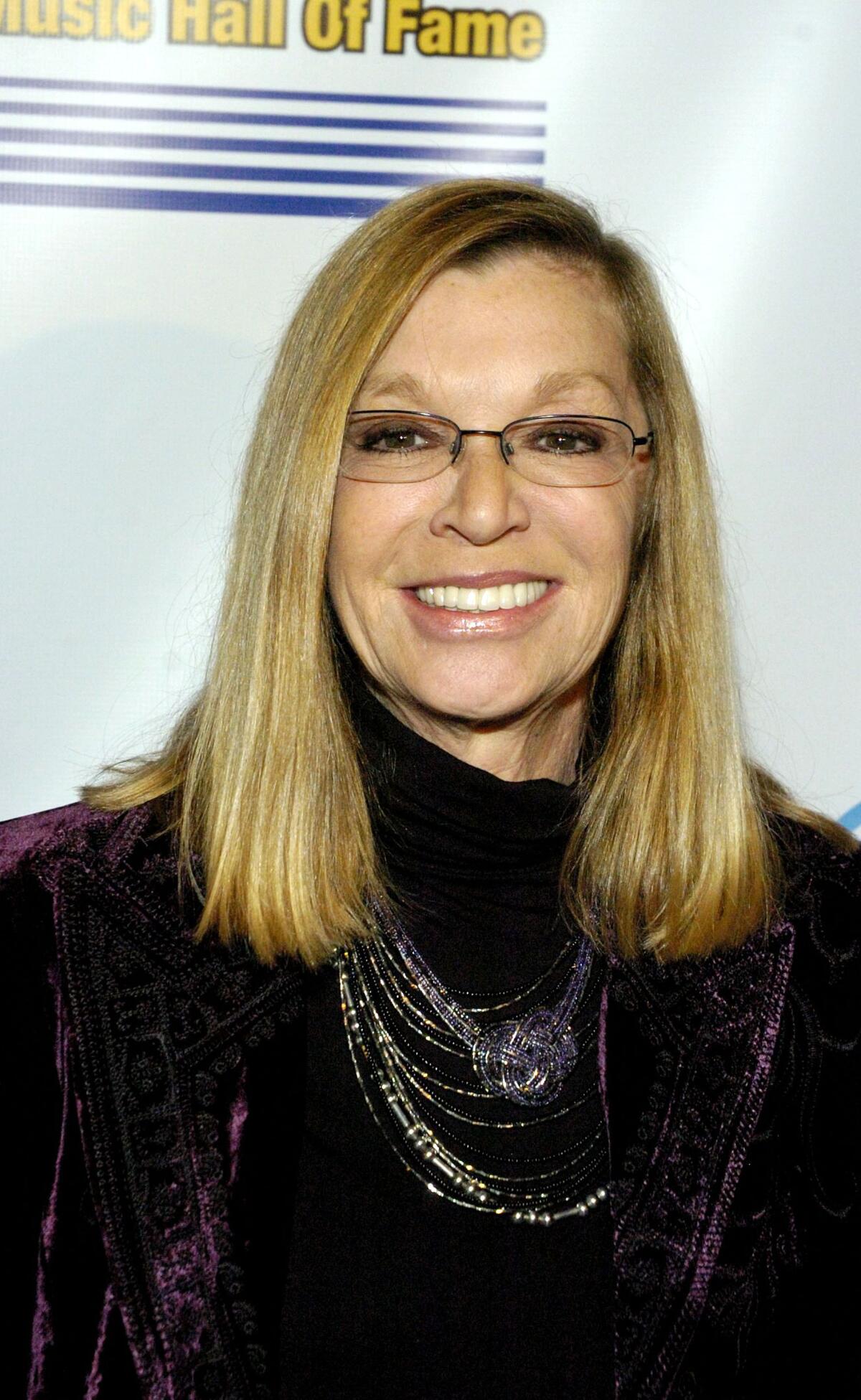 A woman in long brown hair and wearing a black outfit smiles.