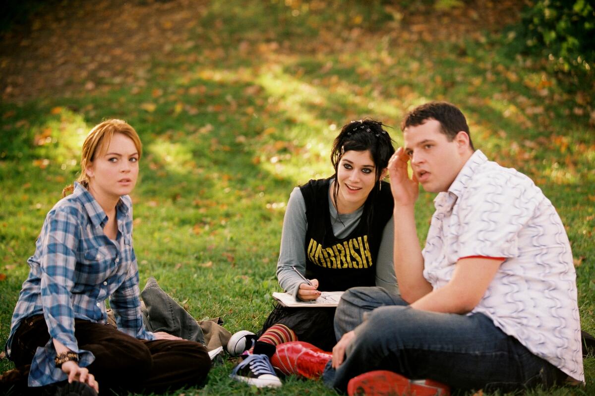 High school students, two female and one male, sit outdoors on the ground