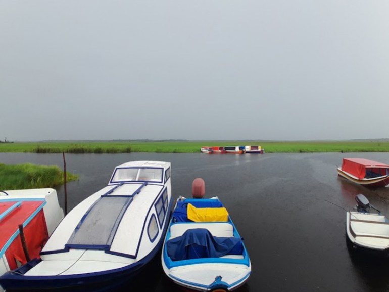 Small boats sit docked at Wakapoa, a disputed region of Guyana. Behind them, a river and marshland are visible.