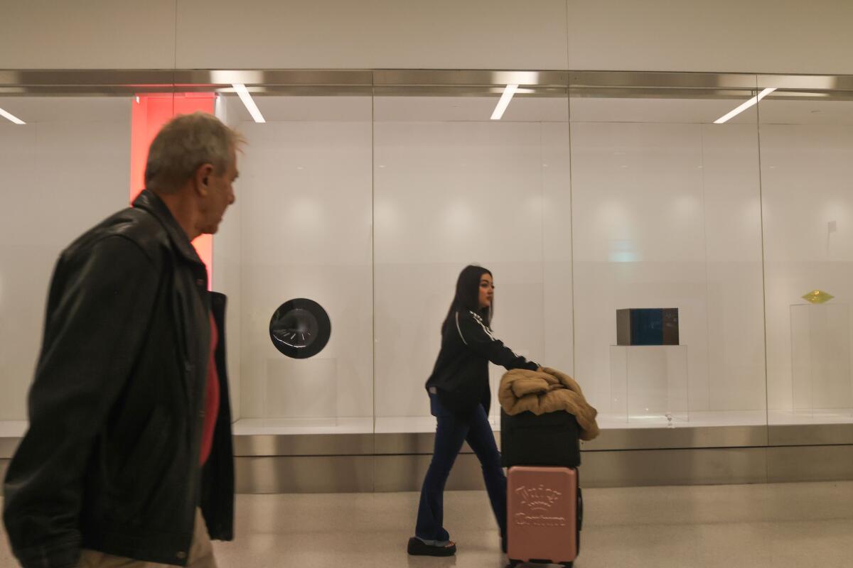 People with luggage walk by an art exhibit at LAX.