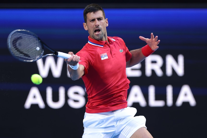 A man dressed in red swings for a tennis ball with a racquet.