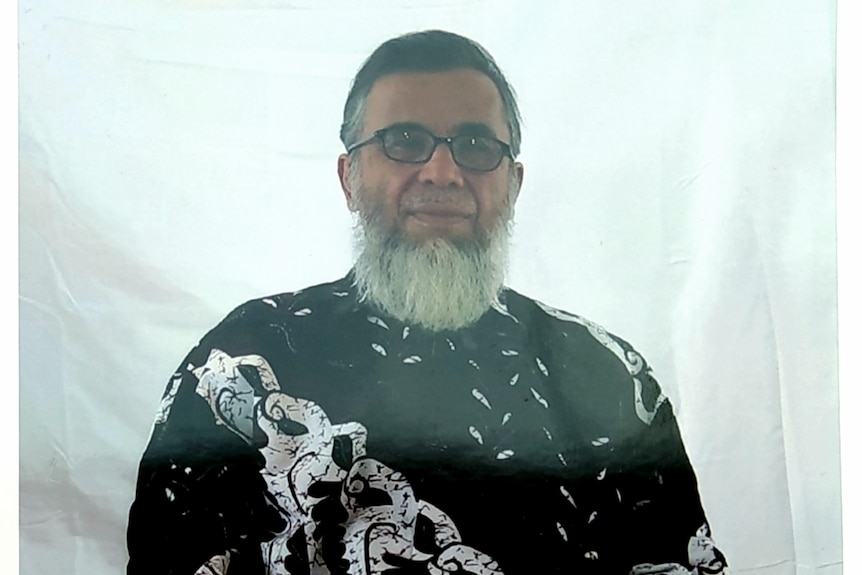 A bespectacled middle aged Indonesian man with a grey beard but no moustache wears a black and white top.