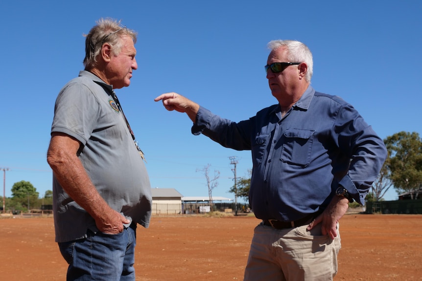 two men talk to each other on a dusty unused block