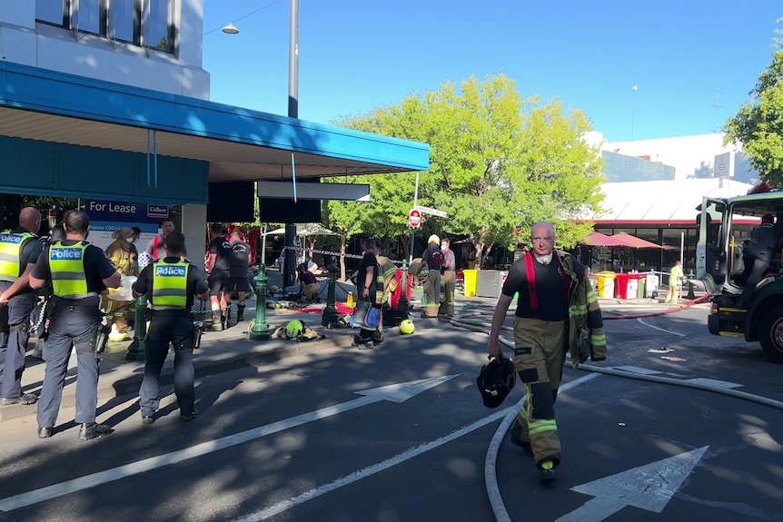 Police wearing yellow high-vis vests gather on the street around a storefront.