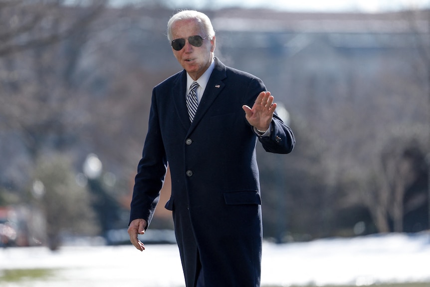 A man in aviators waves while walking through snow