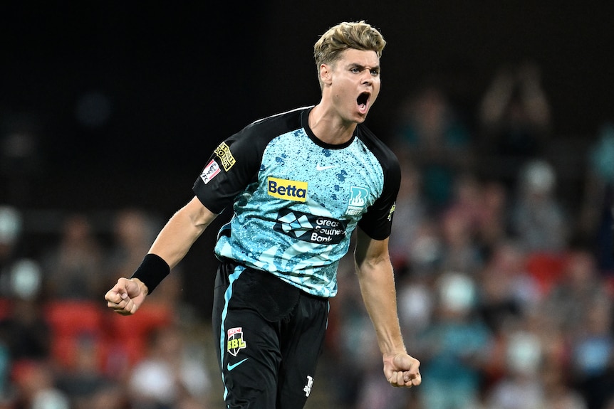 A male cricketer, wearing teal and black, running and celebrating after taking a wicket