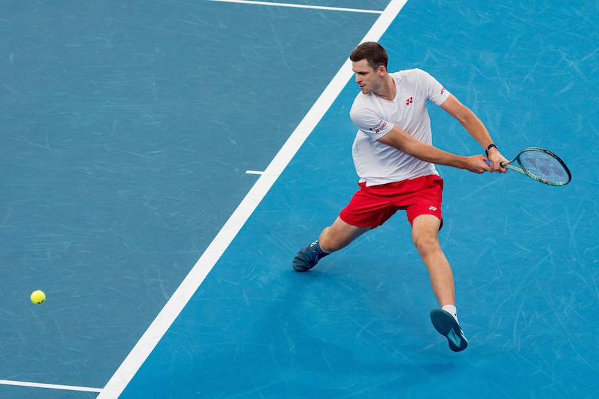 A Polish tennis player looks down at the court as he steps to his side and gets ready for a backhand.