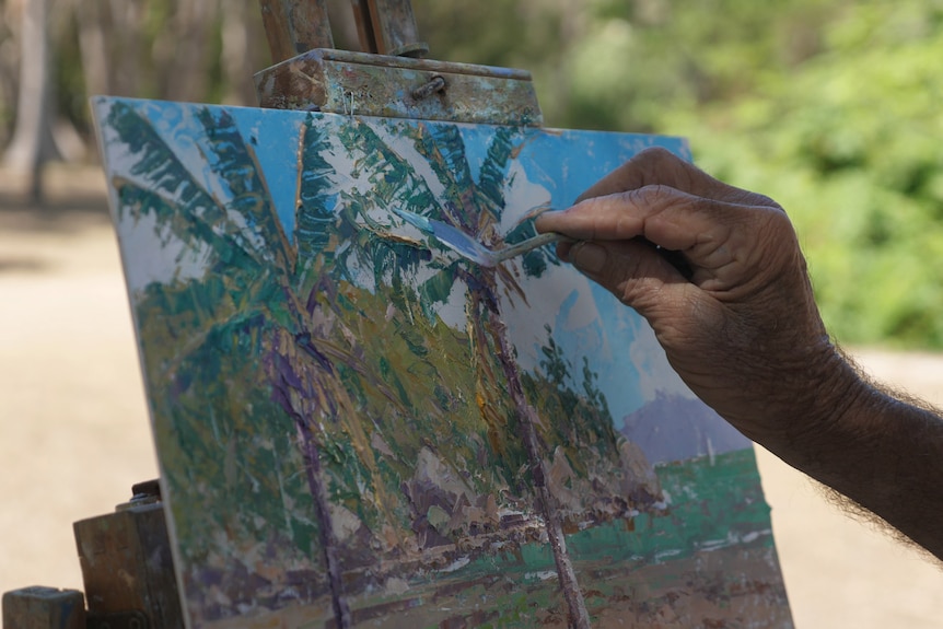 Close up of a hand painting on a small canvas outdoors