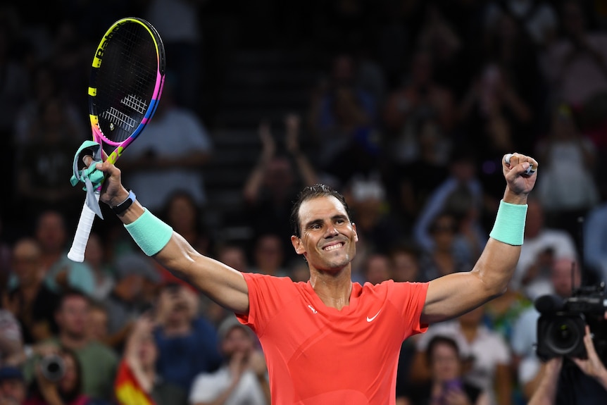 Rafael Nadal  holds up his tennis raquet and arms and smiles.