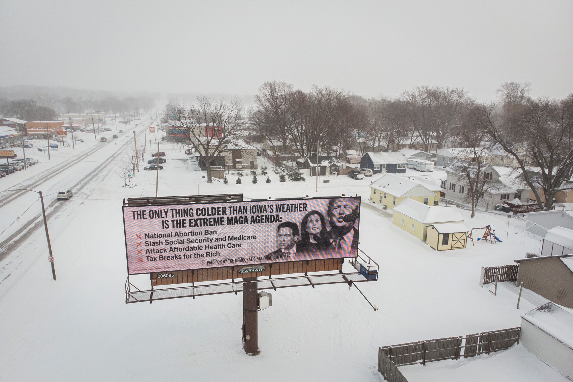 A billboard near a snow covered city says 'the only thing colder than Iowa's weather is the extreme MAGA agenda' and shows Republican candidates' faces.