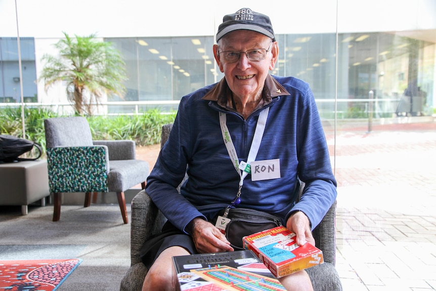 An older man holds board games in a library.